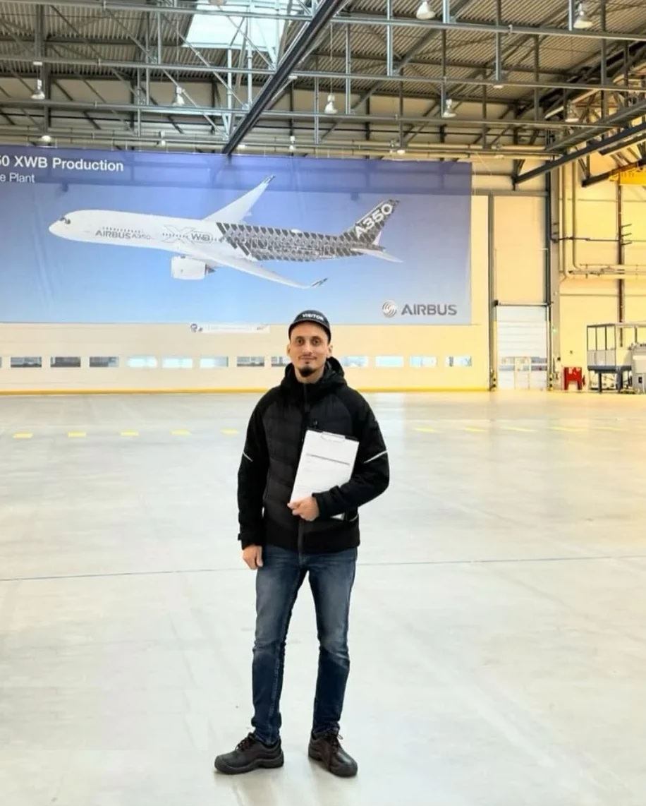 Der Inhaber der Meisterstapler Akademie mit Klemmbrett in einer Halle des Airbus-Werks Stade, im Hintergrund ein A350-Banner